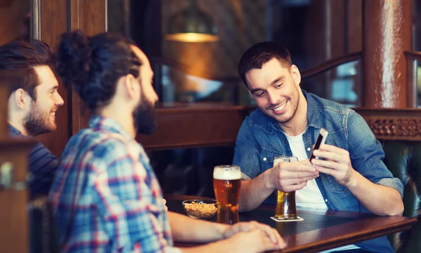 Male friends with smartphone drinking beer at bar — Stock Photo, Image