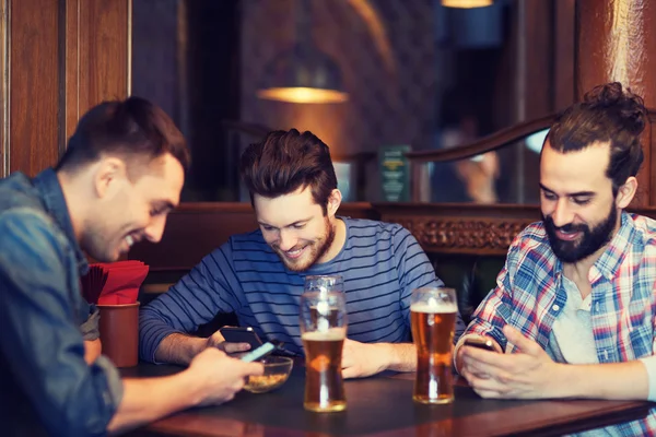 Чоловіки друзі зі смартфонами п'ють пиво в барі — стокове фото