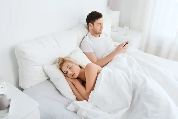 Homem mensagem de texto enquanto a mulher está dormindo na cama — Fotografia de Stock