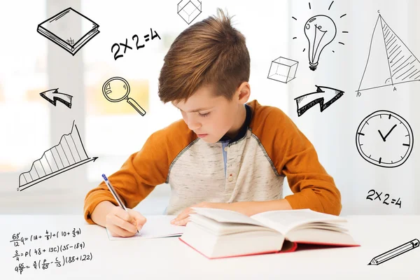 Estudante menino com livro escrevendo para notebook em casa — Fotografia de Stock