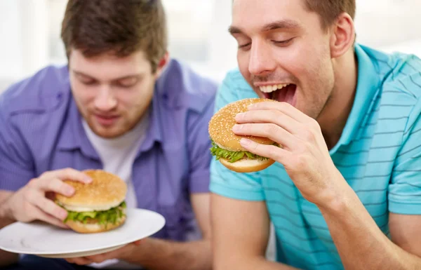 Close up of friends eating hamburgers at home — Stock Photo, Image