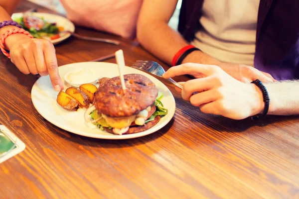 Primer plano de amigos manos compartiendo hamburguesa en el bar — Foto de Stock