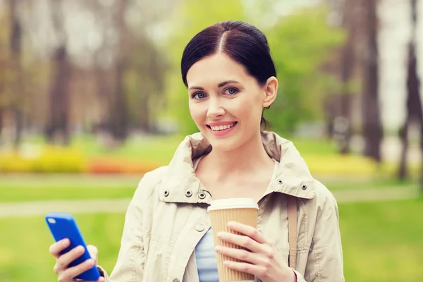 Smiling woman with smartphone and coffee in park — Stock Photo, Image