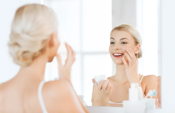 Mujer feliz aplicando crema a la cara en el baño — Foto de Stock