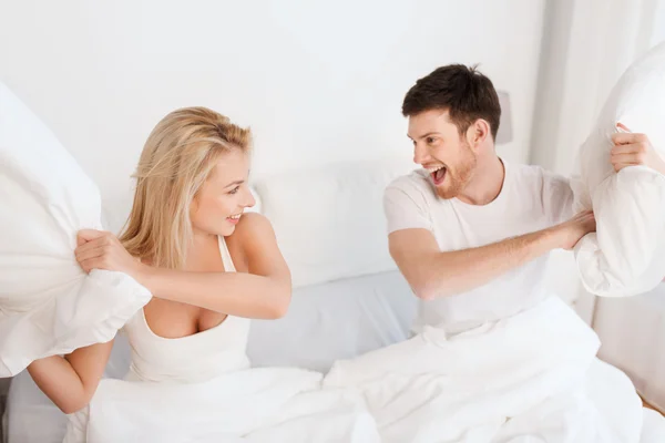 happy couple having pillow fight in bed at home