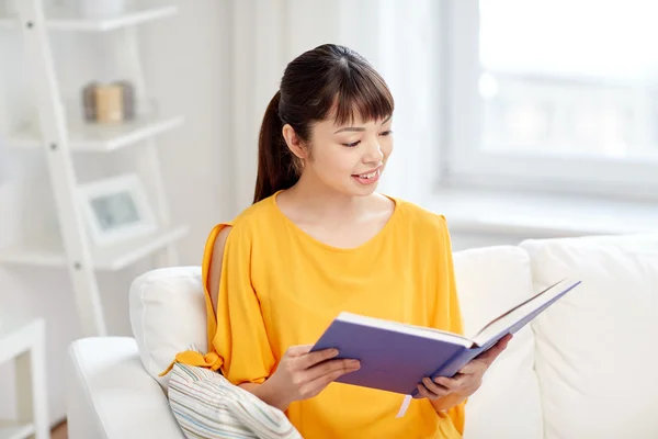 Улыбающаяся молодая азиатка читает дома книгу — стоковое фото