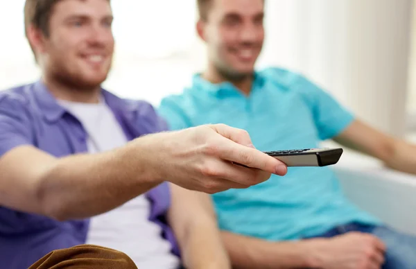 Amigos masculinos felices con control remoto viendo la televisión en casa — Foto de Stock