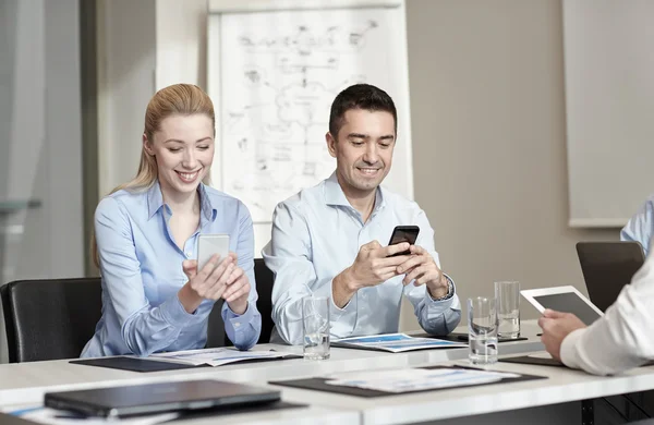 Pessoas de negócios sorridentes com smartphones no escritório — Fotografia de Stock