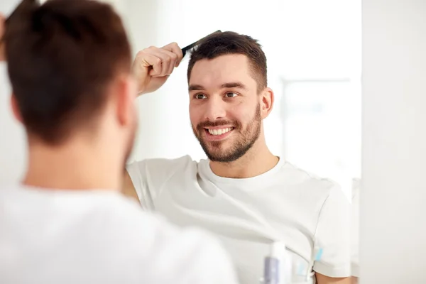 Homem feliz escovando o cabelo com pente no banheiro — Fotografia de Stock