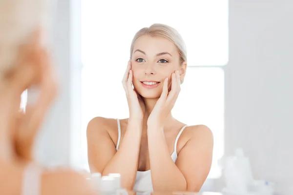 Happy young woman looking to mirror at bathroom — Stock Photo, Image