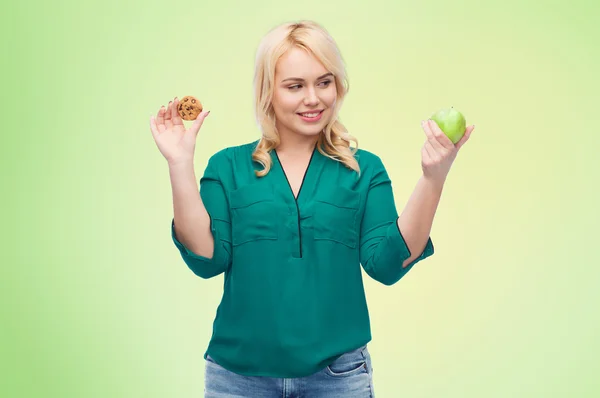 Mulher sorrindo escolher entre maçã e biscoito — Fotografia de Stock