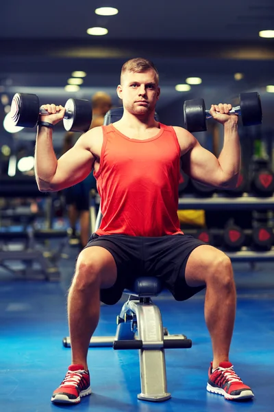 Молодой человек с гантелями, напрягающий мышцы в спортзале — стоковое фото