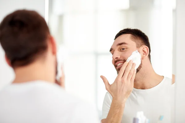 Uomo felice che applica schiuma da barba allo specchio del bagno — Foto Stock