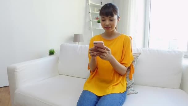 Счастливая азиатка со смартфоном дома — стоковое видео