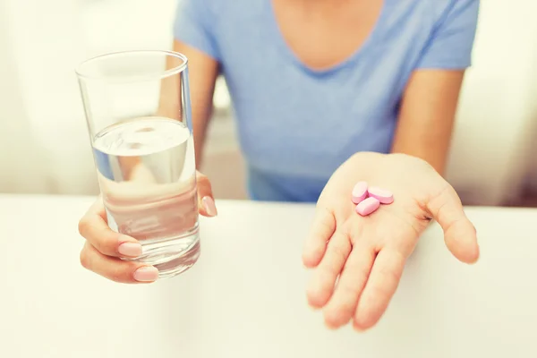 Close up de mãos de mulher com pílulas e água — Fotografia de Stock