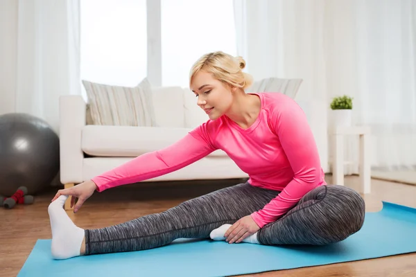 Lycklig kvinna sträcker benet på matta hemma — Stockfoto