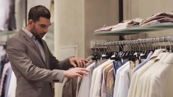 Happy young man choosing clothes in clothing store — Stock Video