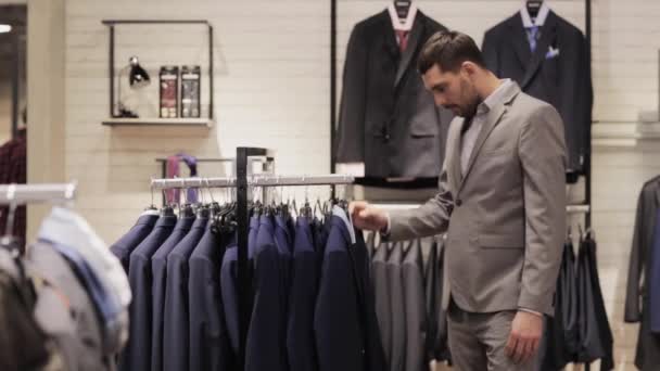 Joven hombre elegir ropa en tienda de ropa — Vídeo de stock