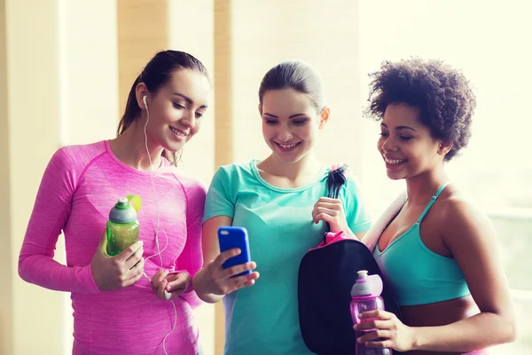 Mujeres felices con botellas y smartphone en el gimnasio — Foto de Stock