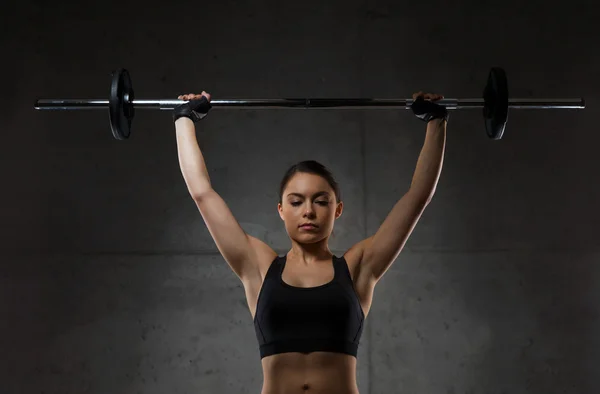 Jovem mulher flexionando músculos com barbell no ginásio — Fotografia de Stock