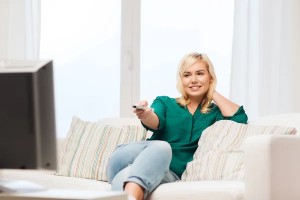 Sonriente mujer con control remoto viendo la televisión en casa — Foto de Stock