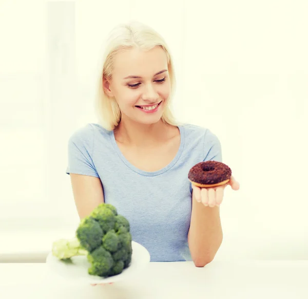 Uśmiechnięta kobieta z brokuły i pączek w domu — Zdjęcie stockowe