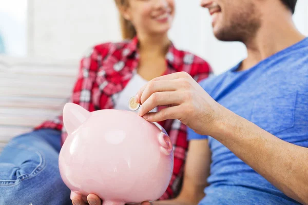 Close up of happy couple putting coin to piggybank — Stock Photo, Image