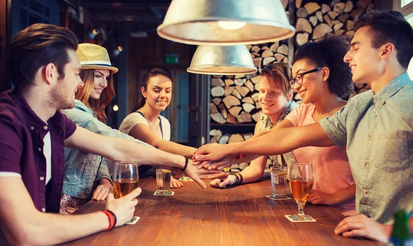 Amici felici con bevande e mani in alto al bar — Foto Stock
