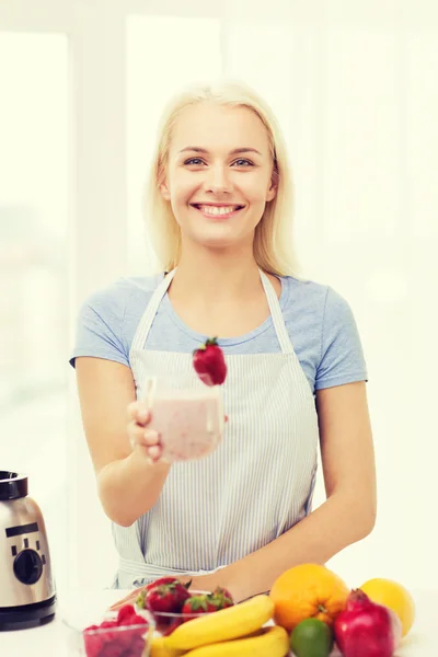 Smiling woman holding glass of fruit shake at home — ストック写真