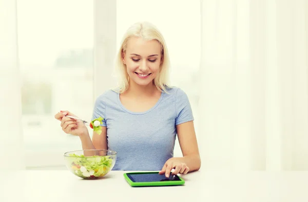 Lachende vrouw eten Salade met tablet pc thuis — Stockfoto