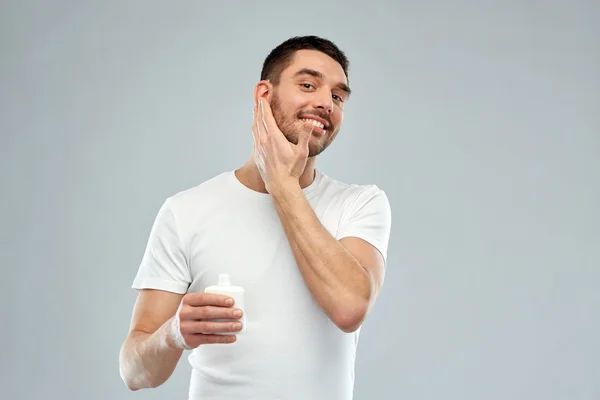 Щасливий молодий чоловік наносить крем або лосьйон на обличчя — стокове фото