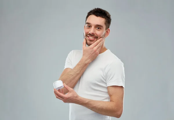 Heureux jeune homme appliquant crème pour faire face sur gris — Photo