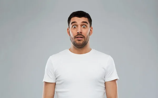 Homem assustado em t-shirt branca sobre fundo cinza — Fotografia de Stock