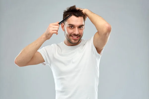 Homem feliz escovando o cabelo com pente sobre cinza — Fotografia de Stock