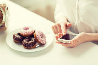 close up of hands with smart phone and donuts clipart
