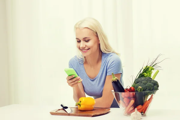 Улыбающаяся женщина со смартфоном готовит овощи — стоковое фото