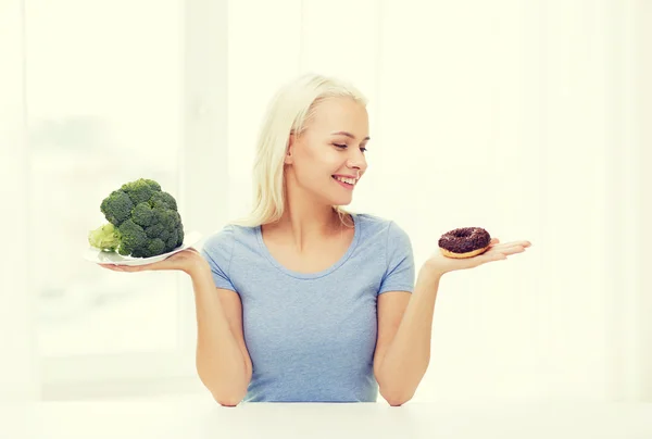 Donna sorridente con broccoli e ciambelle a casa — Foto Stock