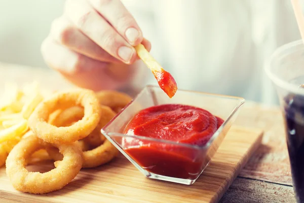 Close up de mão mergulhando batatas fritas em ketchup — Fotografia de Stock