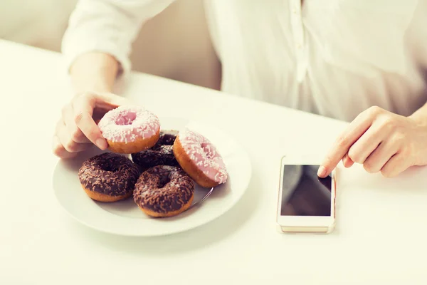 Close up of hands with smart phone and donuts — ストック写真