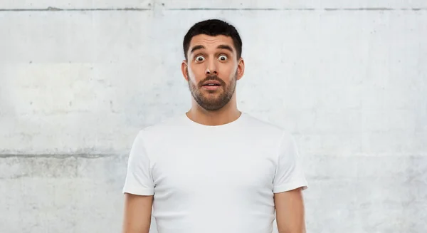 Hombre asustado en camiseta blanca sobre fondo de pared —  Fotos de Stock