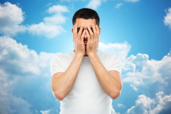 Man in een witte t-shirt die betrekking hebben op zijn gezicht met handen — Stockfoto