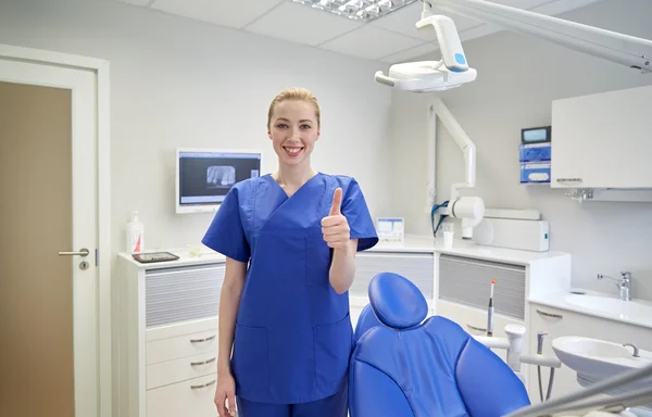 Dentista mujer feliz mostrando pulgares hacia arriba en la clínica —  Fotos de Stock