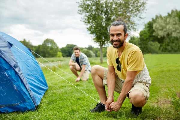 Amigos sorridentes montando tenda ao ar livre — Fotografia de Stock