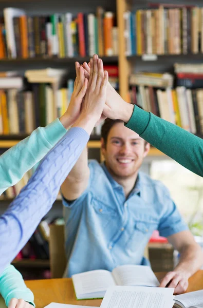 Estudiantes con libros haciendo high five en la biblioteca — Foto de Stock