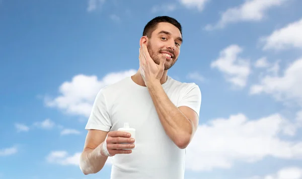 Jovem feliz aplicando creme ou loção no rosto — Fotografia de Stock