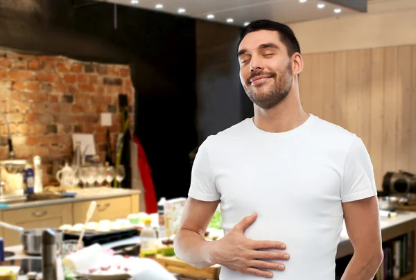 Feliz homem cheio tocando barriga sobre cozinha — Fotografia de Stock