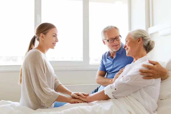 Familia feliz visitando a la mujer mayor en el hospital — Foto de Stock