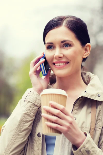 Улыбающаяся женщина со смартфоном и кофе в парке — стоковое фото