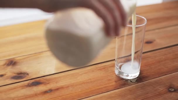 Mano verter la leche en el vaso sobre la mesa de madera — Vídeo de stock