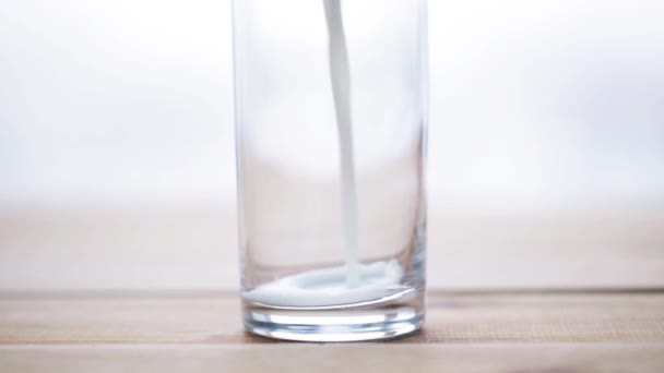 Молоко, наливаемое в пустой стакан на деревянном столе — стоковое видео